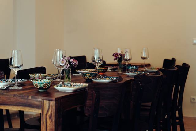 Gastraum von Mana Mana: lange Holztafel, gedeckt mit Weingläsern, bunt bemalten Schalen und kleinen Blumensträußen